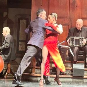 A couple dancing tango at a show. The man wore a black suit and the woman wore a red dress